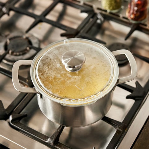 Een pan staat op het kooktoestel, met eten erin en glazen deksel erop