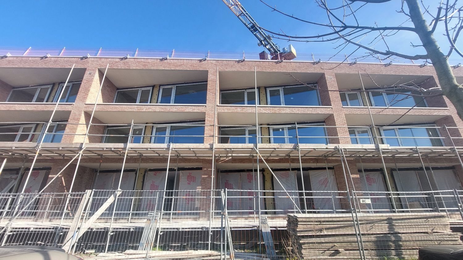 Foto van gevel van appartementengebouw in steigers met de nieuwe gevelsteentjes in rozebruine kleur