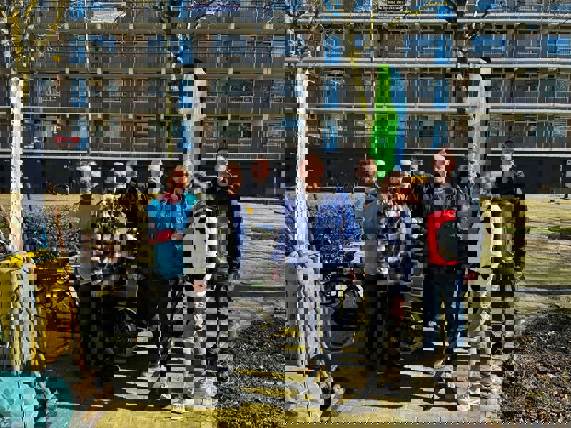 Groepsfoto voor flat Plutostraat met bewoners, wijkbeheerder Woonforte en schone buurt coach erbij